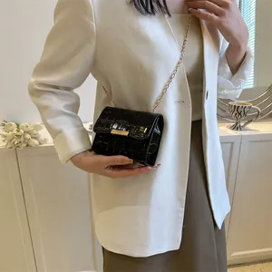 Detail of black glossy crocodile pattern crossbody bag with elegant gold chain and lock