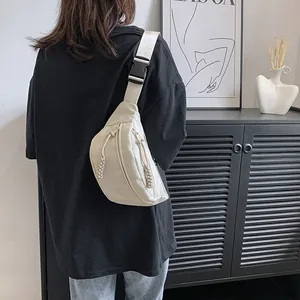 Minimalistische beige nylon borsttas met verstelbare riem gedragen door een model thuis