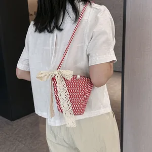Sac bandoulière tressé rouge et blanc avec nœud en dentelle et perle porté par mannequin