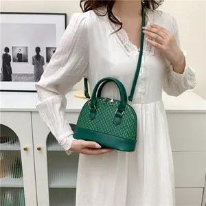 Petit sac coquille vert foncé avec texture tressée, porté en bandoulière élégante