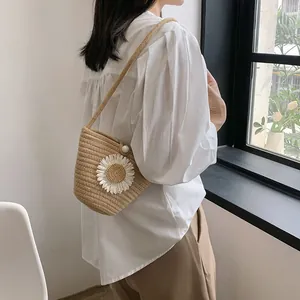 Détail d'un sac seau en paille avec marguerites et fermoir perle porté par un mannequin