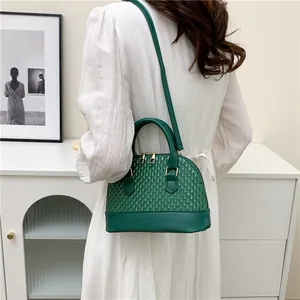 Détail du sac coquille vert foncé avec texture tissée porté sur une robe blanche