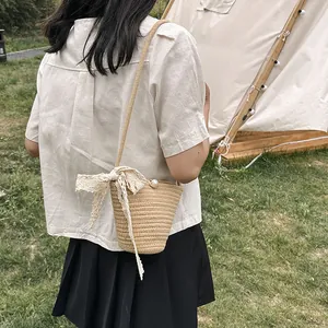 Détail du sac seau en paille tressée avec nœud en dentelle et perle sur fond d'herbe