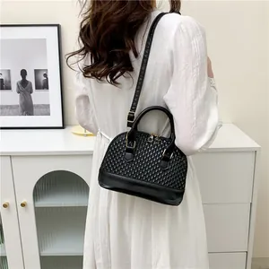 Détail d'un sac bandoulière noir tissé avec garniture dorée porté par un mannequin