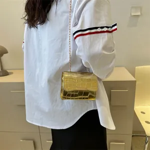 Detail of gold faux crocodile crossbody bag with metallic chain strap worn by a model