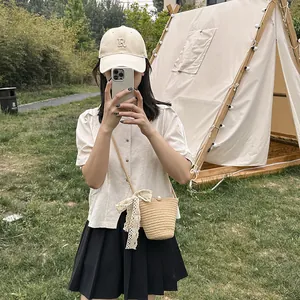 Détail d'un sac seau en paille beige avec nœud en dentelle blanche et perle en extérieur