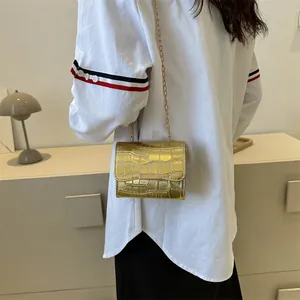 Detail showing gold crossbody bag with crocodile texture and shiny chain strap on model