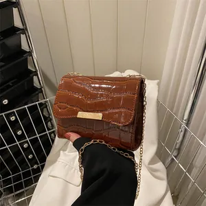 Detailed view of dark brown crocodile pattern leather and gold metal buckle on flap bag