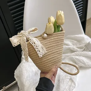 Détail du sac seau en paille tressée avec un nœud en dentelle blanche et un fermoir perle