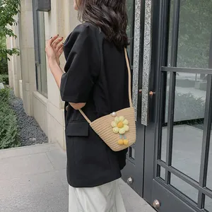 Detail of hand-woven straw bucket bag featuring a yellow floral ornament and pearl clasp