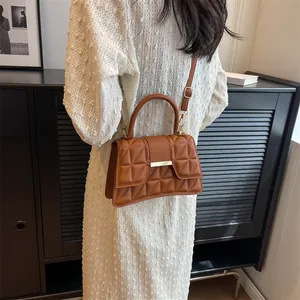 Brown quilted crossbody bag on model wearing white dress in elegant indoor setting