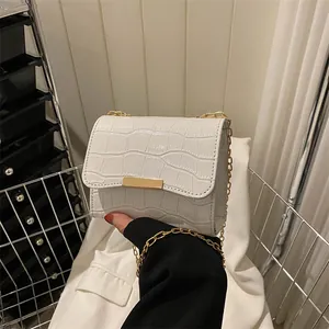 Detail of white crocodile pattern crossbody bag featuring golden chain and metal trim
