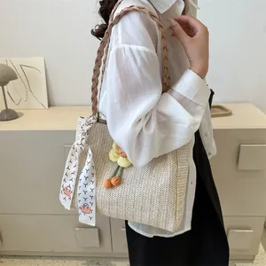 Détail d'un sac seau en paille tressée beige avec un foulard rouge et un charme de fleur jaune