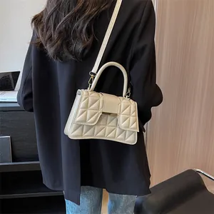 Detail view of cream quilted shoulder bag with triangle patterns and metal buckle