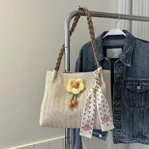 Détail d'un sac seau en paille tressée avec breloque fleurie et écharpe décorative en soie