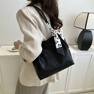 Detail of black tote bag with embossed texture, braided strap, and decorative scarf