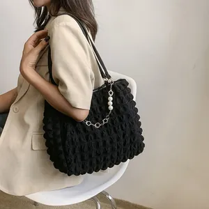 Detail of black bubble texture tote bag with pearl and floral metal chain accessory