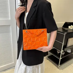 Détail du sac bandoulière en cuir verni orange avec texture géométrique et chaîne dorée