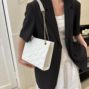 Gros plan d'un sac à bandoulière matelassé blanc avec chaîne dorée porté par un mannequin