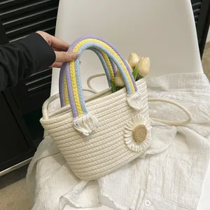Détail d'un sac seau en paille beige avec anses arc-en-ciel et fleur de marguerite