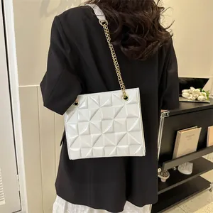 Détail d'un sac bandoulière blanc avec gaufrage géométrique et fine chaîne dorée