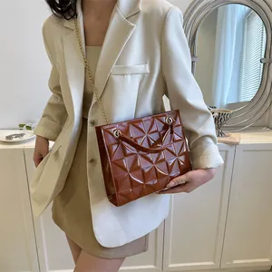Détail d'un sac marron à gaufrage géométrique avec chaîne dorée et fini en cuir verni