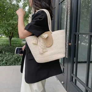 Detail of woven straw bucket bag with lace bow and brown leather strap on shoulder