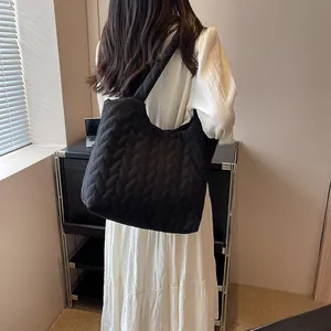 Detail of black quilted shoulder bag with braided texture on a model wearing white dress
