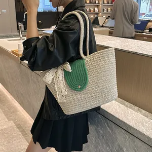 Detail of hand-woven straw tote bag with green contrast flap and white lace bow decoration