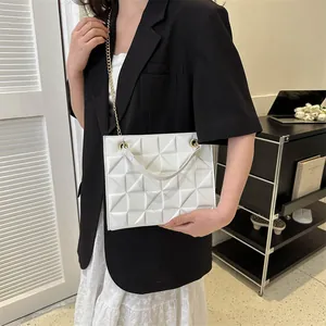 Sac bandoulière blanc matelassé avec chaîne dorée porté par un mannequin dans un salon