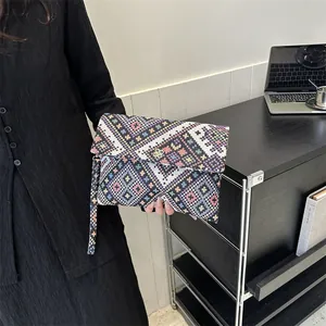 Detail of colorful geometric woven envelope clutch bag with floral metal clasp and strap