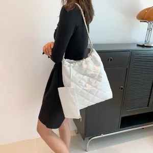 Detail of white quilted tote bag featuring chain straps and a matching small pouch