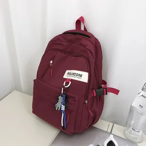 Détail du sac à dos bordeaux avec boucle latérale, patch logo et breloque petit ours