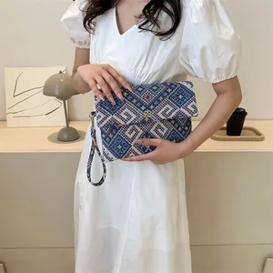 Detail of geometric woven envelope clutch bag with gold flower buckle and wrist strap