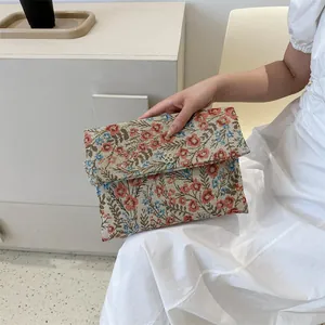 Detail of floral tapestry envelope clutch with a gold clover clasp and textured fabric