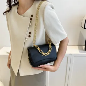 Sac à bandoulière en cuir noir avec chaîne dorée porté avec un blazer beige chic