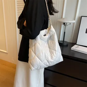 Macro detail of white quilted puffy tote bag featuring gold-toned chain and woven shoulder strap