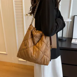 Brown quilted nylon tote bag with metal chain strap shown in a cozy indoor setting