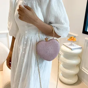 Pink glitter heart-shaped clutch bag with gold handle and chain on a white dress model