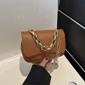 Détail d'un sac à bandoulière en cuir marron avec chaîne dorée décorative et logo minimaliste