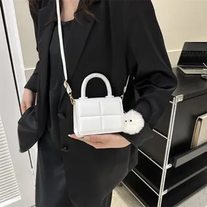 Detail of white quilted handbag with pompom charm and elegant gold-tone hardware accents