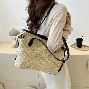 Dettaglio di una borsa tote in paglia con finiture in pelle nera indossata a spalla