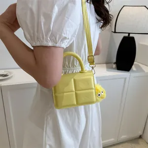 Detail of light yellow mini handbag featuring textured geometric pattern and plush charm