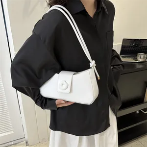 Close-up of white underarm bag with knot strap detail and round embossed buckle