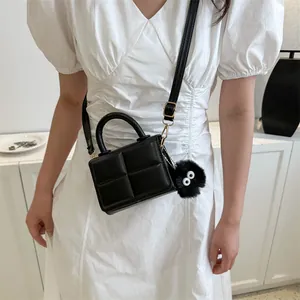 Quilted black crossbody bag detail with plush charm and adjustable strap on white dress