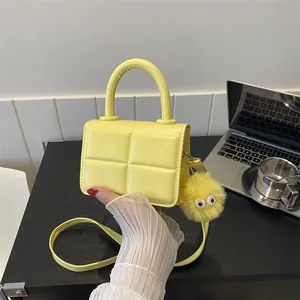 Macro detail of yellow mini square bag with grid texture and yellow plush charm accessory