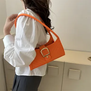 Close-up of bright orange quilted leather baguette bag with a gold square buckle