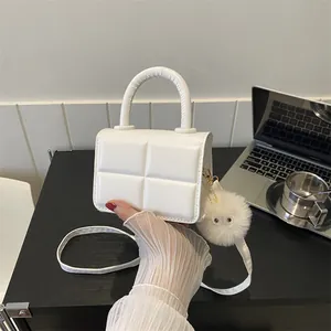 Close-up of a white quilted mini handbag with a cute plush charm and crossbody strap