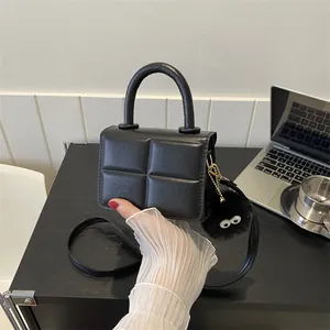 Detail of black quilted mini handbag featuring a cylinder handle and a cute eye bag charm