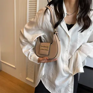 Detailed view of beige crescent shoulder bag with gold clasp worn over a white shirt